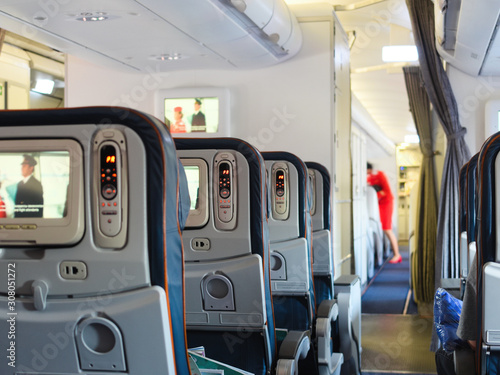 Cabin airliner, blue leather seats with multimedia system, passage between the seats. blurred background, flight attendant doing pre-flight training