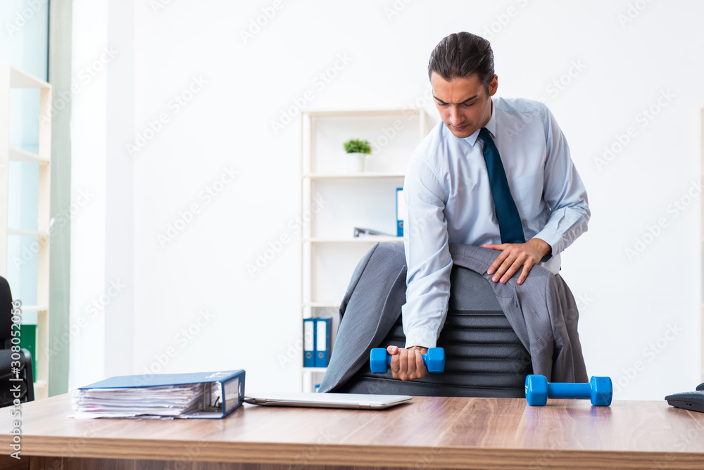 Young handsome employee doing sport exercises at workplace Young handsome employee doing sport exercises at workplace
