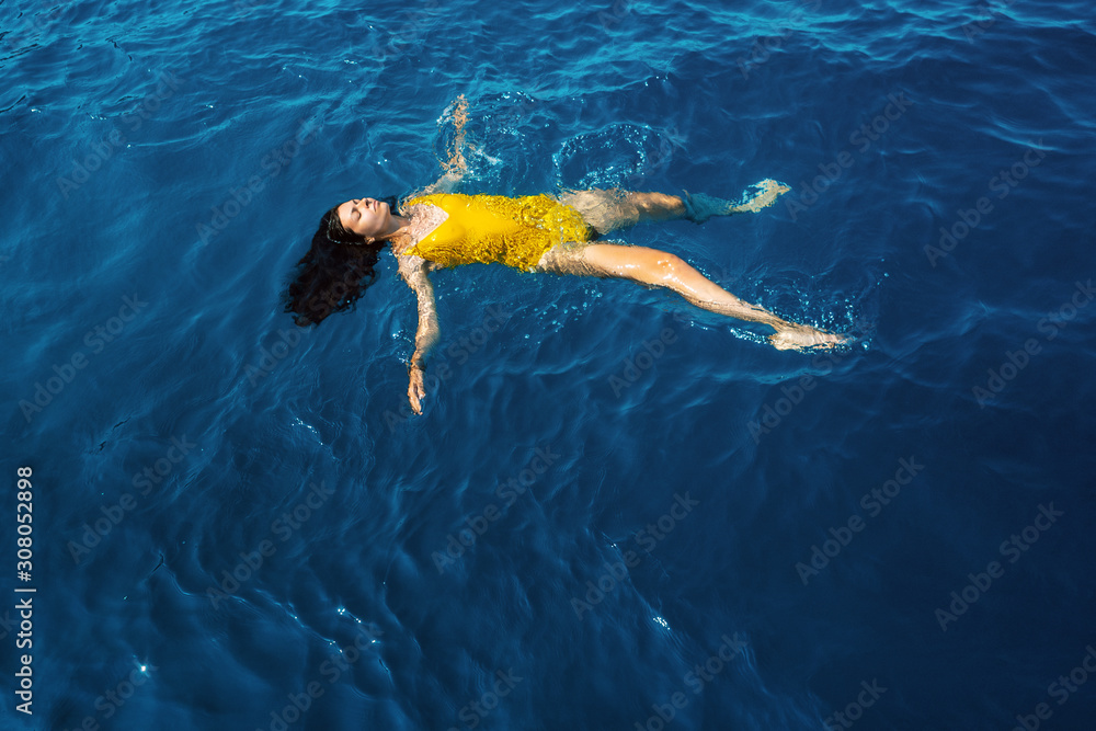 young woman in a one-piece yellow swimsuit floats on the surface of the water.