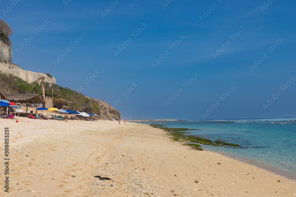 BALI / INDONESIA - OCTOBER 25, 2019: Wide sand Melasti beach with tourists, umbrellas and beds.