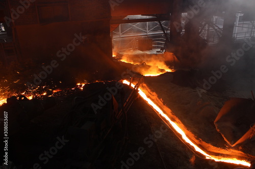 Hot red molten iron flowing in the canal in iron factory with smokes