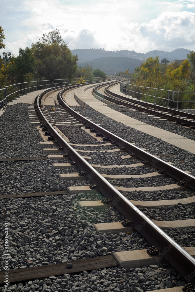 Fototapeta premium Rail tracks on a gravel bed meandering towards the hills.