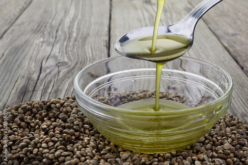 Foto Pouring hemp oil into glass bowl and hemp seeds on wooden background