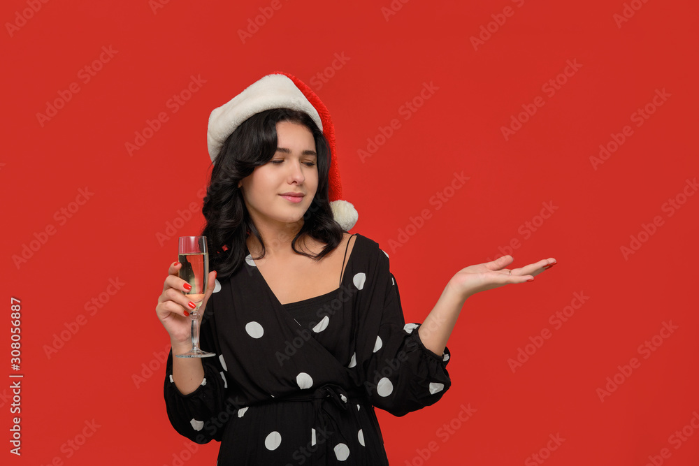 Girl in a black dress and Santa hat with glass of champagne in one hand and copy space on another Girl in a black dress and Santa hat with glass of champagne in one hand and copy space on another