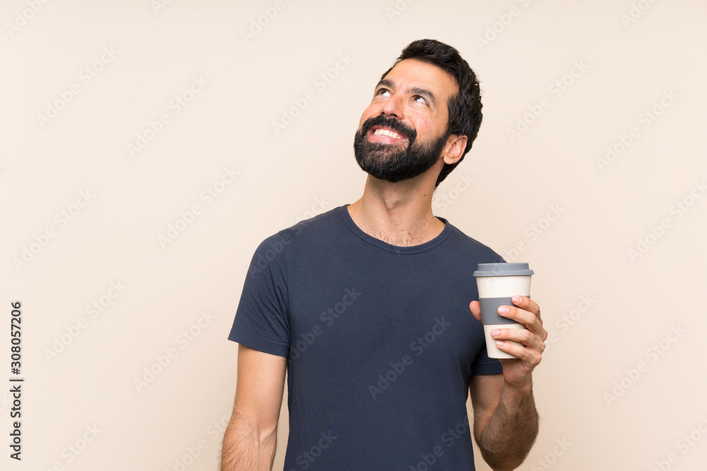 Man with beard holding a coffee looking up while smiling Man with beard holding a coffee looking up while smiling