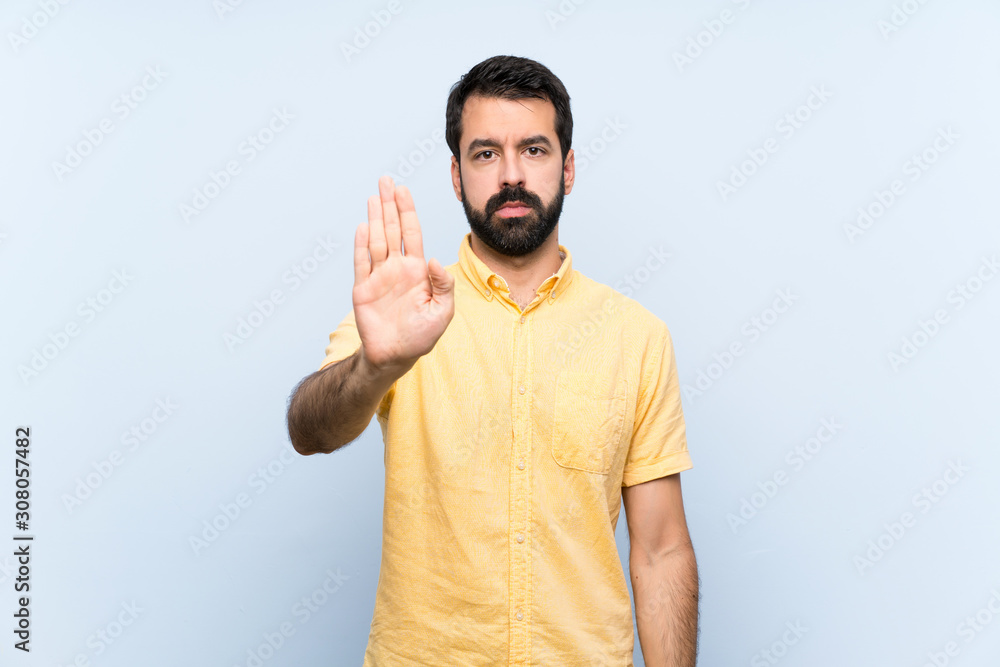 Young man with beard over isolated blue background making stop gesture Young man with beard over isolated blue background making stop gesture