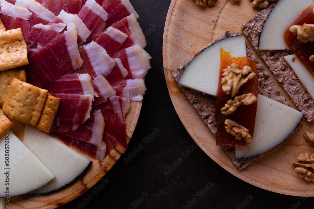 Variety of wood plates with freshly jamon, cheese and roasted bread; a whole cheese and toasted bread with cheese, nuts and quince jelly. Variety of wood plates with freshly jamon, cheese and roasted bread; a whole cheese and toasted bread with cheese, nuts and quince jelly.