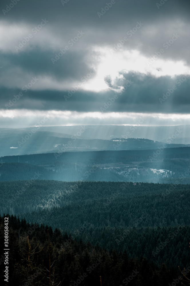 Dramatic nature winter weather sky with clouds and sun light rays and wide panorama mountain view. Brocken, Harz National Park Mountains in Germany