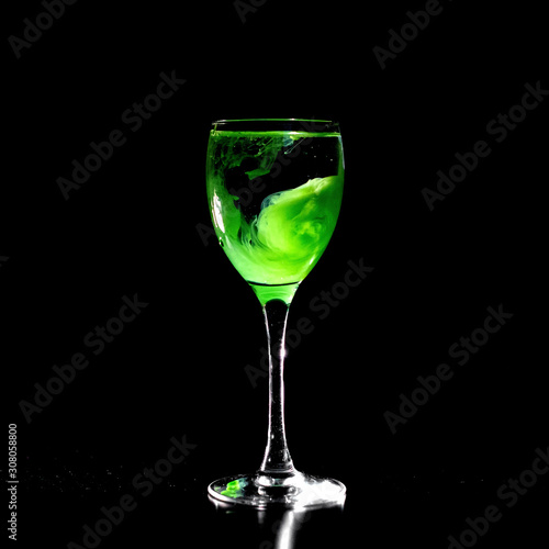 Glass on black background with bizarre pattern of green paint blurred in water. Odd drink, water witch, witchcraft.