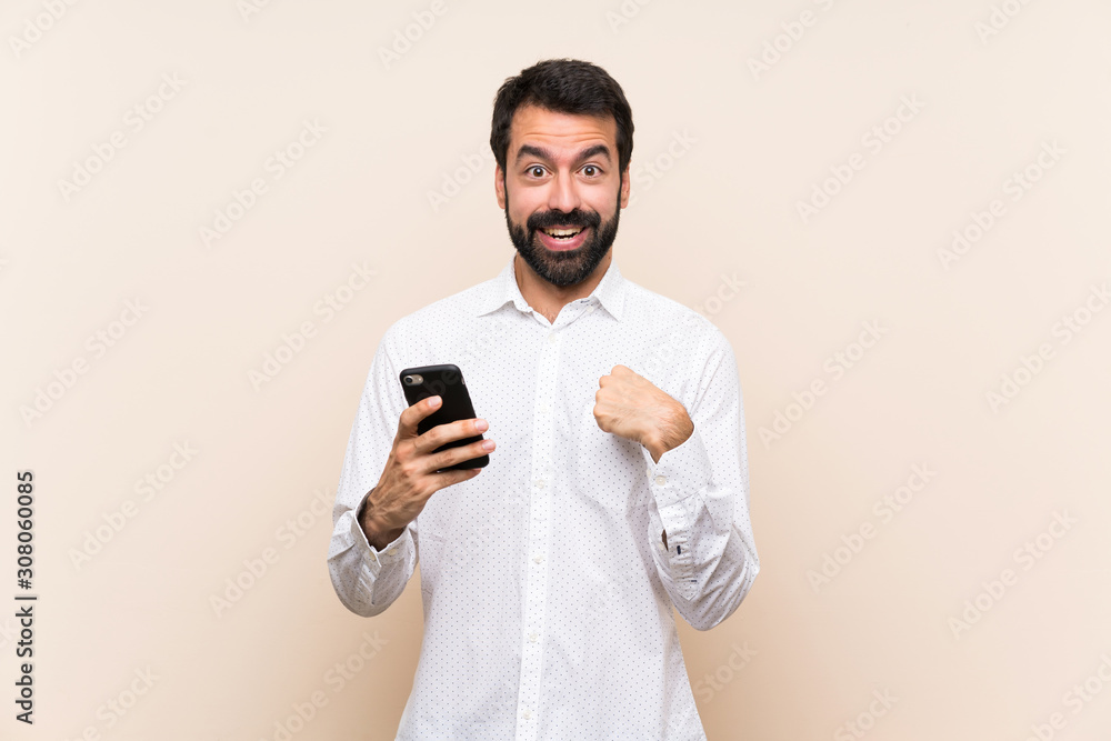 Young man with beard holding a mobile with surprise facial expression Young man with beard holding a mobile with surprise facial expression
