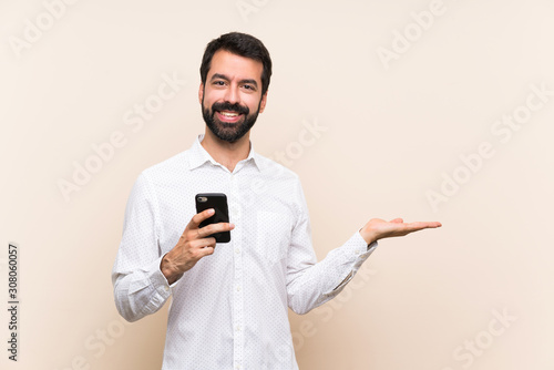 Young man with beard holding a mobile holding copyspace imaginary on the palm to insert an ad