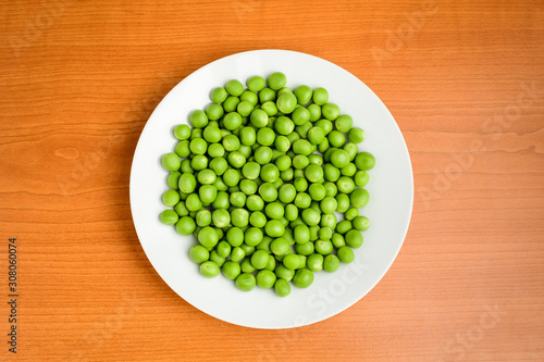 Fresh organic green peas in a white round bowl on a wooden table in soft focus, top view or flat lay of healthy raw vegan food
