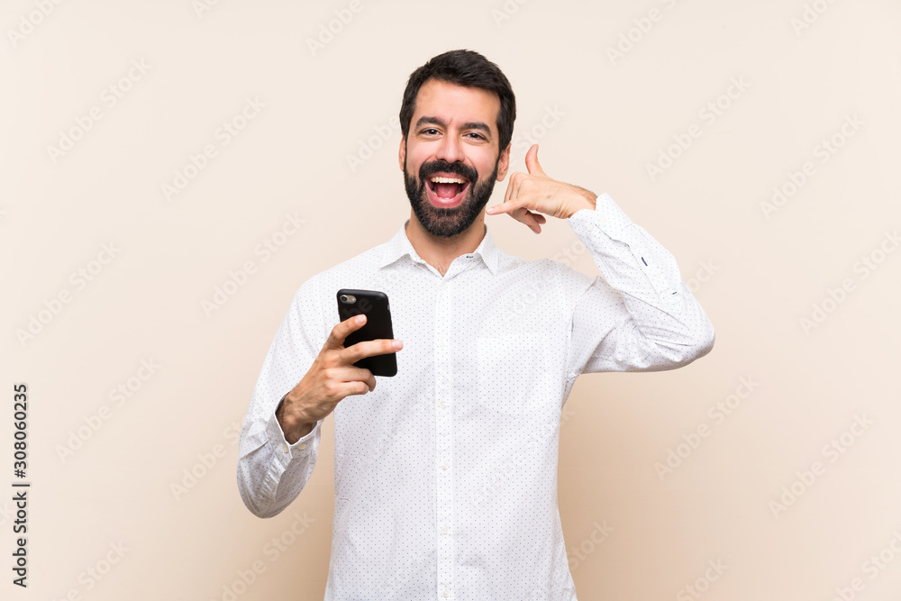 Young man with beard holding a mobile making phone gesture. Call me back sign Young man with beard holding a mobile making phone gesture. Call me back sign