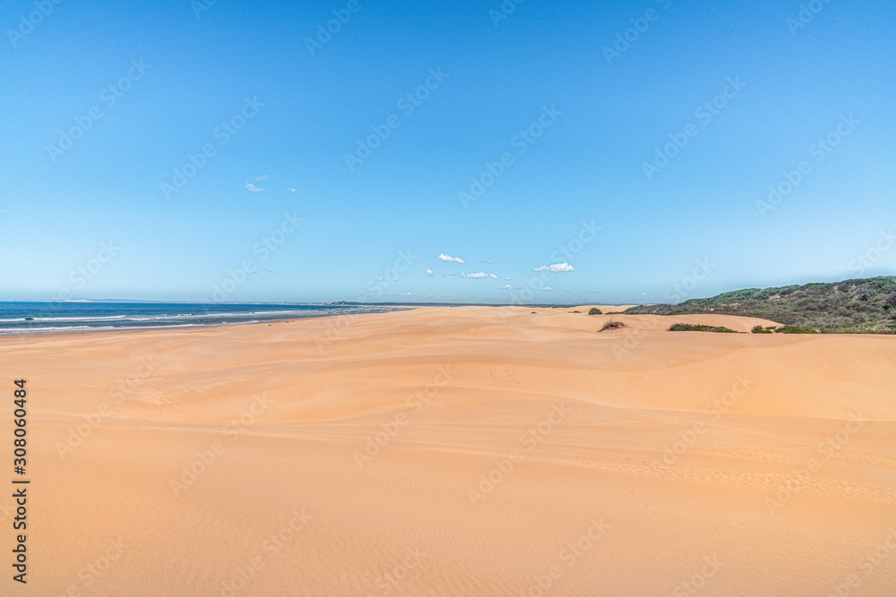 Sandstrand mit Himmel und kleinen Wolken Meer auf der linken Seite Büsche auf der Rechtenseite ein sonniger Tag