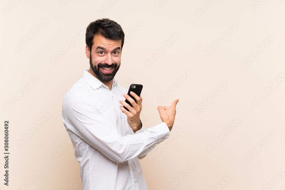 Young man with beard holding a mobile pointing back Young man with beard holding a mobile pointing back