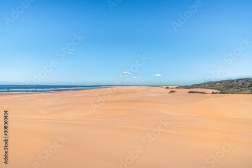 Sandstrand mit Himmel und kleinen Wolken Meer auf der linken Seite Büsche auf der Rechtenseite ein sonniger Tag