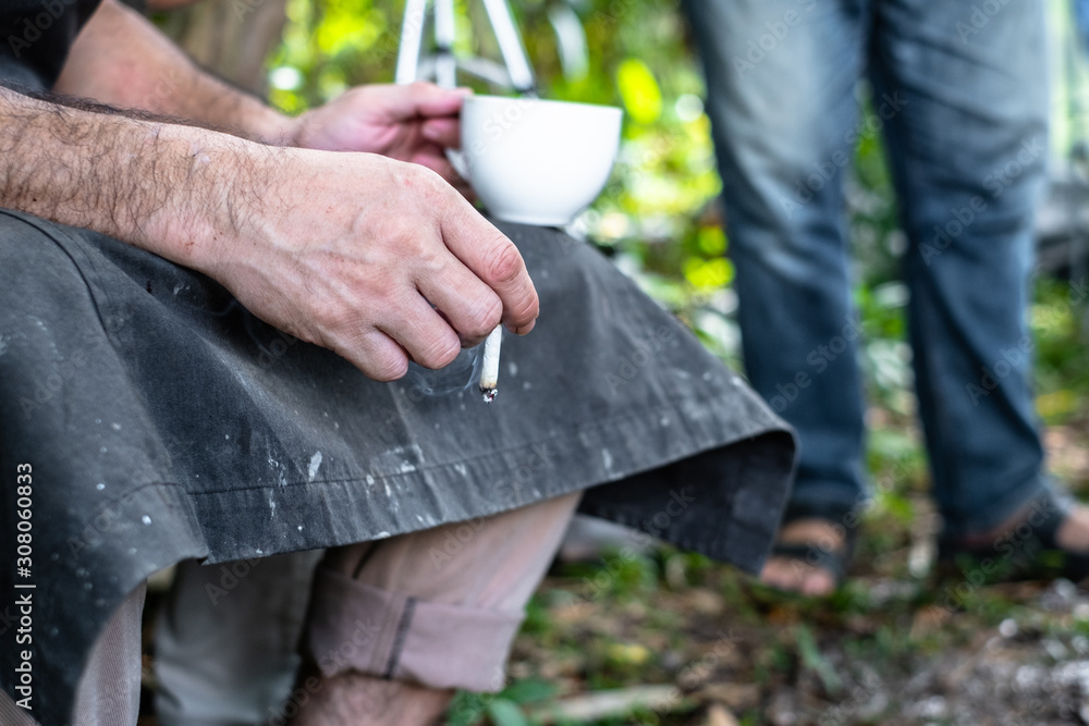 Close up of male hand holding a cigarette and a white cup of coffee. Close up of male hand holding a cigarette and a white cup of coffee.