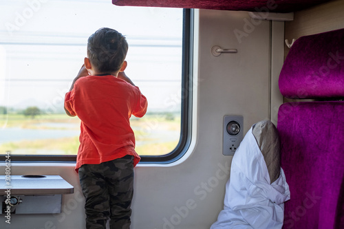 Back view of happy little boy oooking out through wide glass window of a train. Child traveling by railway. photo