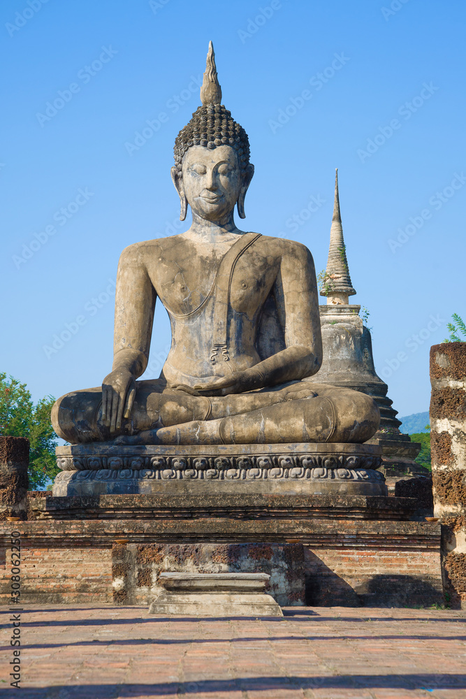 Fototapeta premium Ancient sculpture of a sitting Buddha close-up on a background of blue sky. The ruins of the Buddhist temple of Wat Chana Songkhram. Sukhothai, Thailand