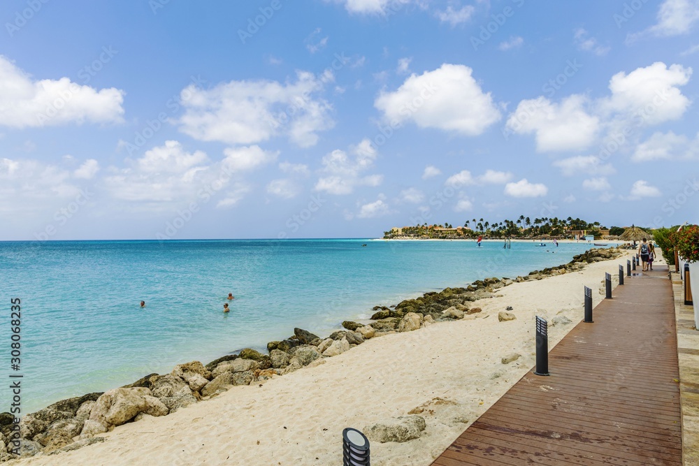 Fototapeta premium Beautiful view of white sand Aruba beach. Blue sunbeds under sun umbrellas on turquoise water and blue sky with white clouds background. Caribbean. Atlantic ocean. Aruba.