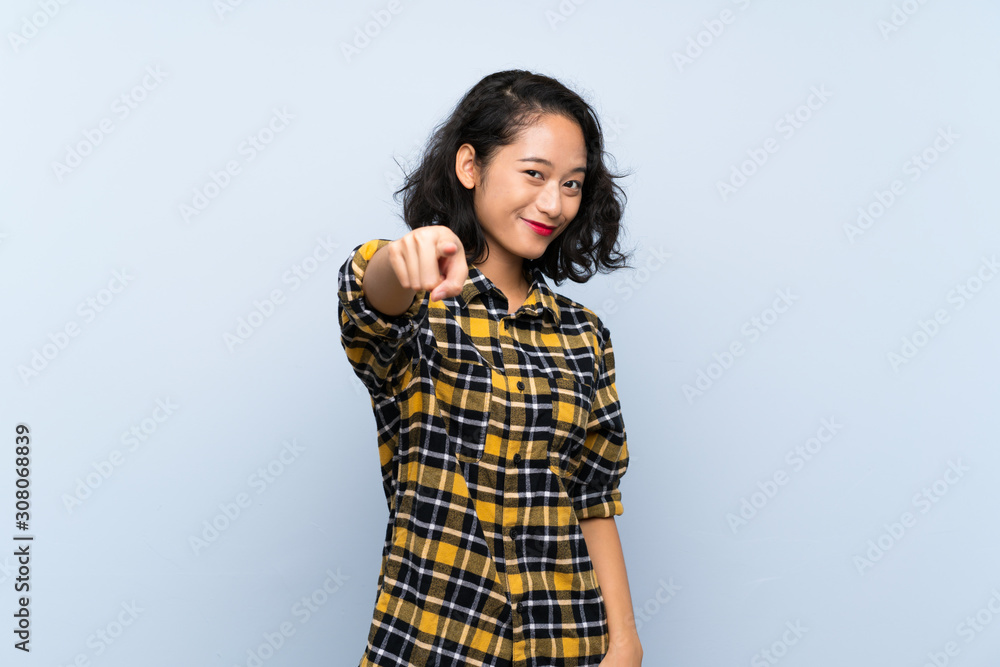 Asian young woman over isolated blue background points finger at you with a confident expression Asian young woman over isolated blue background points finger at you with a confident expression