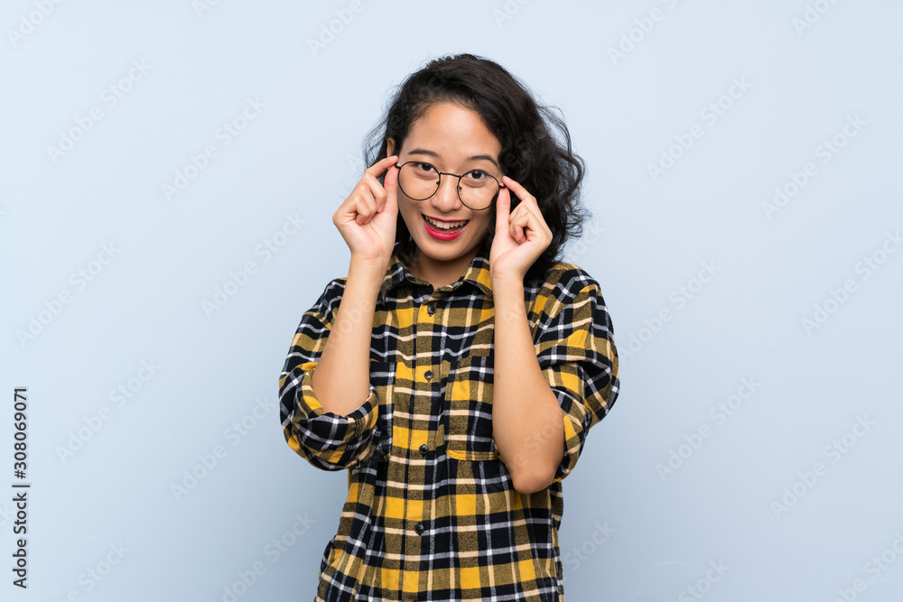Asian young woman over isolated blue background with glasses and surprised Asian young woman over isolated blue background with glasses and surprised