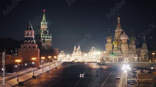 Beautiful panorama of Moscow Red Square on a calm winter night with the Kremlin clock tower, the Cathedral of Vasily the Blessed and brightly illuminated GUM. Rare cars and pedestrians passing by.