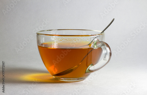 A cup of hot tea and a spoon on a light blurry background.