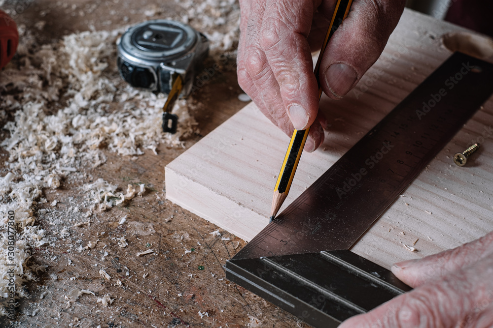 Carpenter making measurements on a table with a pencil and a metal square Carpenter making measurements on a table with a pencil and a metal square