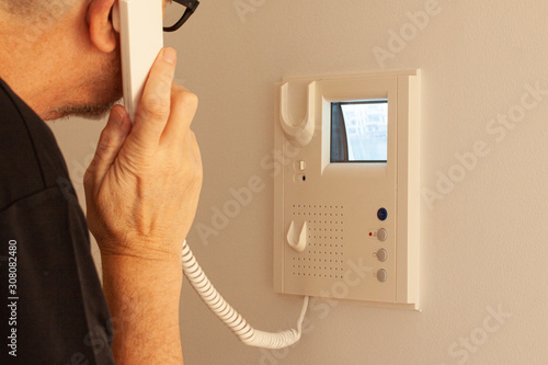 Man answering a call at a door phone while looking at the screen on the CRT display. Video intercom equipment. Selective focus image. photo