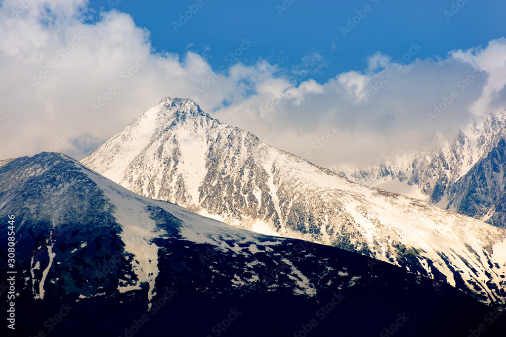 high tatras mountain ridge in springtime. snow capped rocky peaks in dramatic dappled sunlight beneath a clouds on a blue sky. place where earth meets sky concept