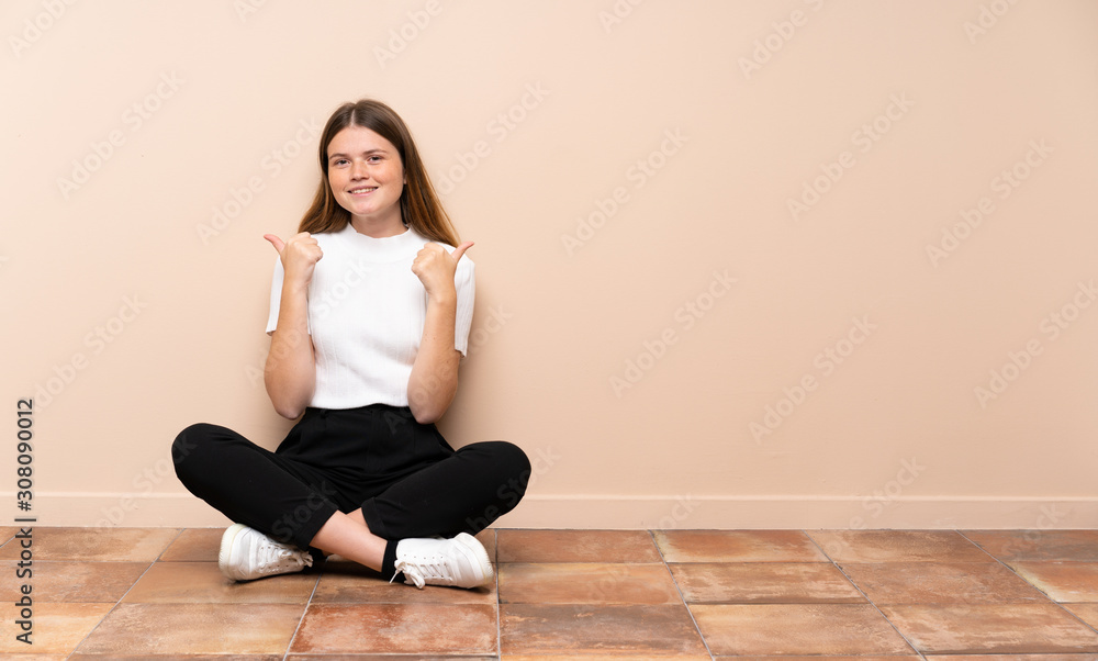 Ukrainian teenager girl sitting on the floor with thumbs up gesture and smiling Ukrainian teenager girl sitting on the floor with thumbs up gesture and smiling