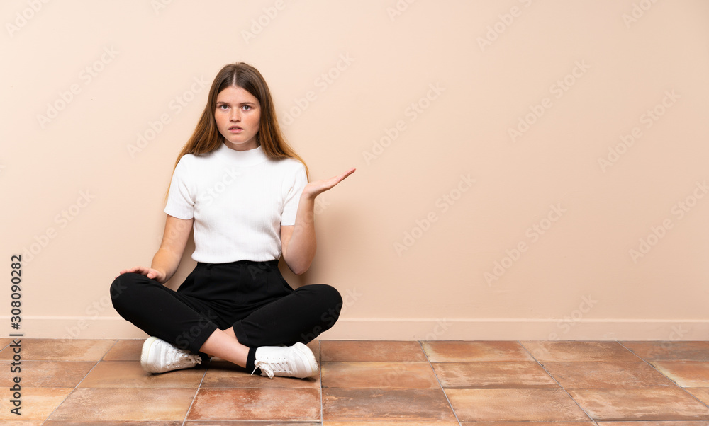 Ukrainian teenager girl sitting on the floor making doubts gesture Ukrainian teenager girl sitting on the floor making doubts gesture