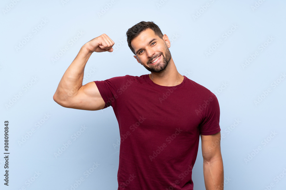 Handsome man over isolated blue background doing strong gesture Handsome man over isolated blue background doing strong gesture