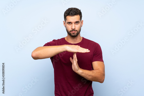 Handsome man over isolated blue background making time out gesture