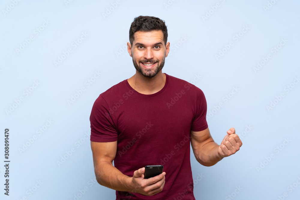 Handsome man over isolated blue background with phone in victory position Handsome man over isolated blue background with phone in victory position