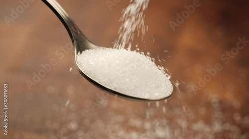 Stack of footage: White sugar fall through teaspoon down on a brown wood background. Slow motion. HD