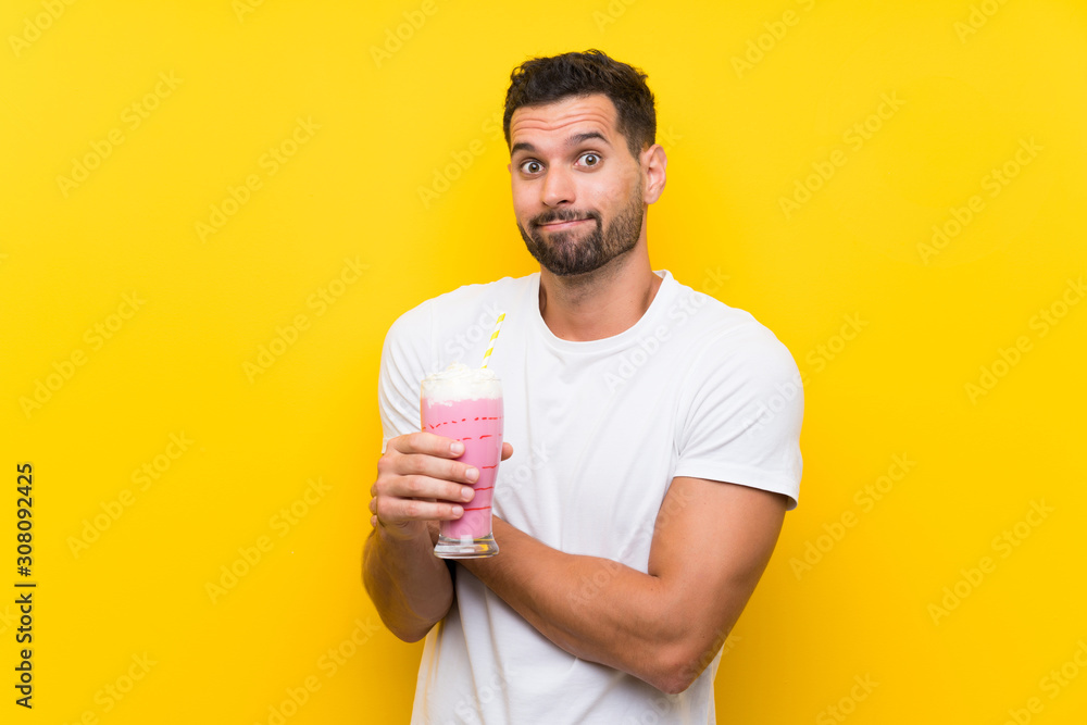 Young man with strawberry milkshake over isolated yellow background making doubts gesture while lifting the shoulders Young man with strawberry milkshake over isolated yellow background making doubts gesture while lifting the shoulders