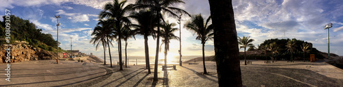 Super wide panorama from the boulevard of Arpoador backlit with silhouetted palm trees in Rio de Janeiro at Devils beach against a blue sky with clouds