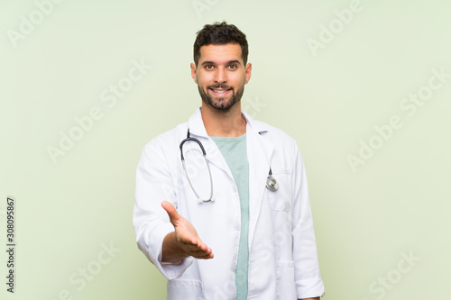 Young doctor man over isolated green wall handshaking after good deal