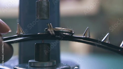 CU: Professional designer sets metal accessory spikes on fashionable black leather choker with press machine closeup photo