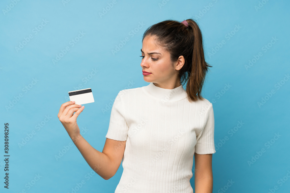 Young brunette girl over isolated blue background holding a credit card Young brunette girl over isolated blue background holding a credit card