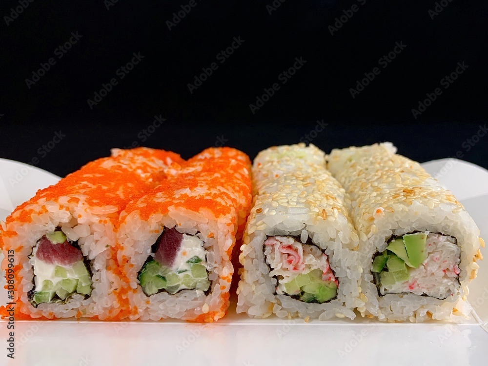 Sushi with red fish and avocado, close-up, on a black background. Japanese traditional cuisine, delicious sushi with dill and sesame seeds. Rolls - California and Philadelphia. Sushi with red fish and avocado, close-up, on a black background. Japanese traditional cuisine, delicious sushi with dill and sesame seeds. Rolls - California and Philadelphia.