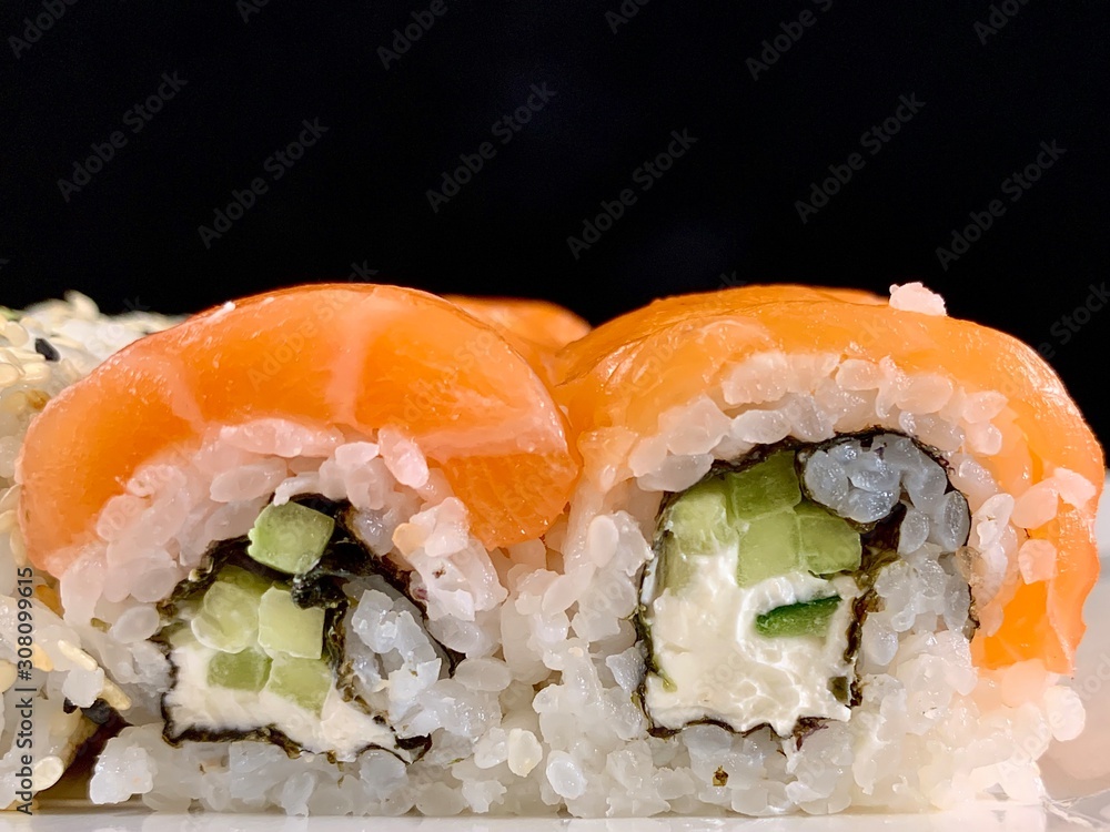 Sushi with red fish and avocado, close-up, on a black background. Japanese traditional cuisine, delicious sushi with dill and sesame seeds. Rolls - California and Philadelphia. Sushi with red fish and avocado, close-up, on a black background. Japanese traditional cuisine, delicious sushi with dill and sesame seeds. Rolls - California and Philadelphia.