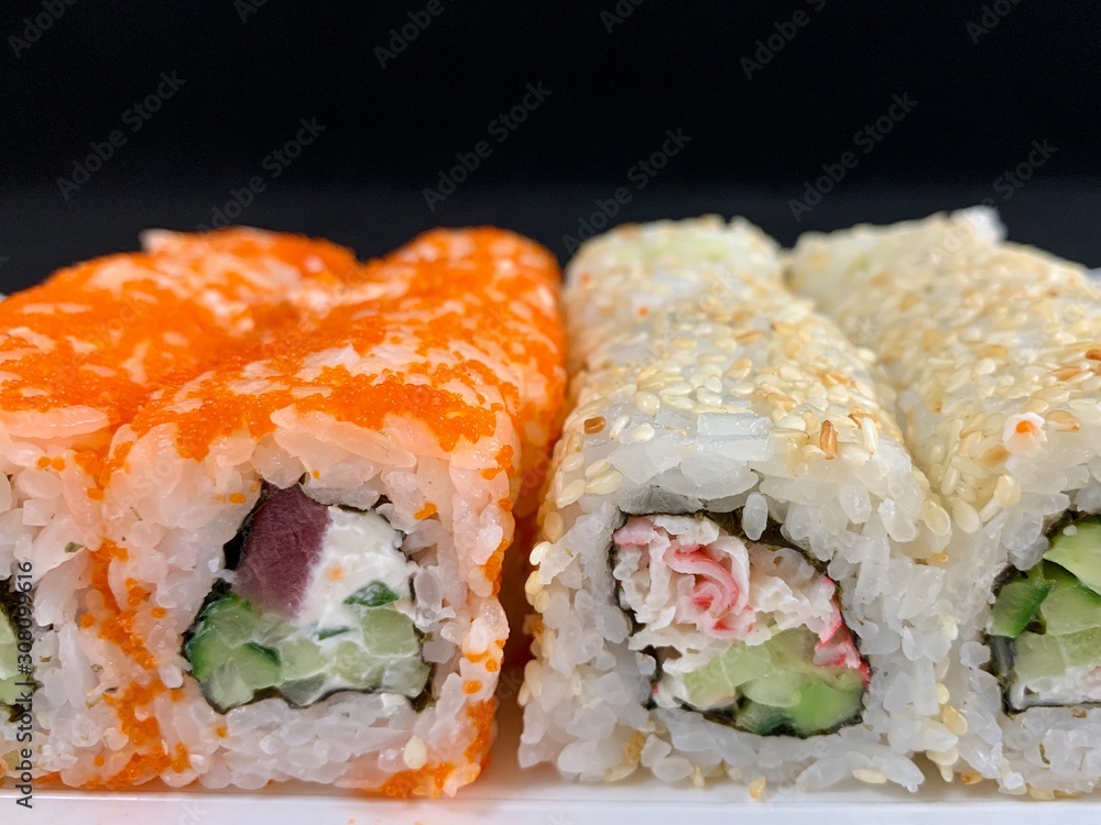 Sushi with red fish and avocado, close-up, on a black background. Japanese traditional cuisine, delicious sushi with dill and sesame seeds. Rolls - California and Philadelphia. Sushi with red fish and avocado, close-up, on a black background. Japanese traditional cuisine, delicious sushi with dill and sesame seeds. Rolls - California and Philadelphia.