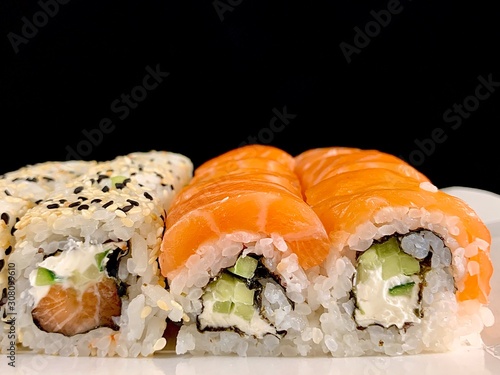 Sushi with red fish and avocado, close-up, on a black background. Japanese traditional cuisine, delicious sushi with dill and sesame seeds. Rolls - California and Philadelphia.