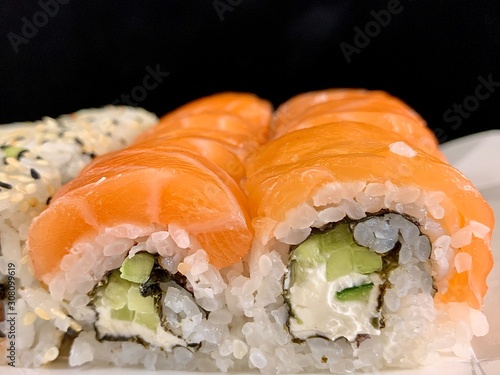 Sushi with red fish and avocado, close-up, on a black background. Japanese traditional cuisine, delicious sushi with dill and sesame seeds. Rolls - California and Philadelphia.