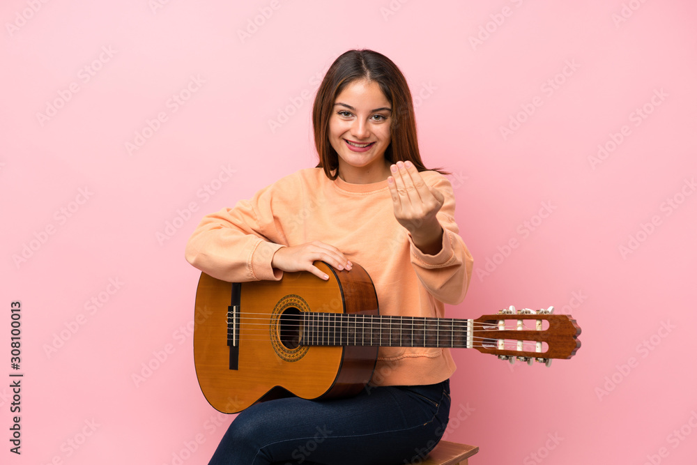 Young brunette girl with guitar over isolated pink background inviting to come with hand. Happy that you came Young brunette girl with guitar over isolated pink background inviting to come with hand. Happy that you came