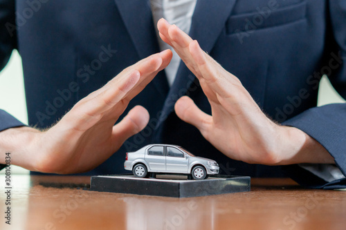 the man hands cover the little car model on the table, the insurance concept