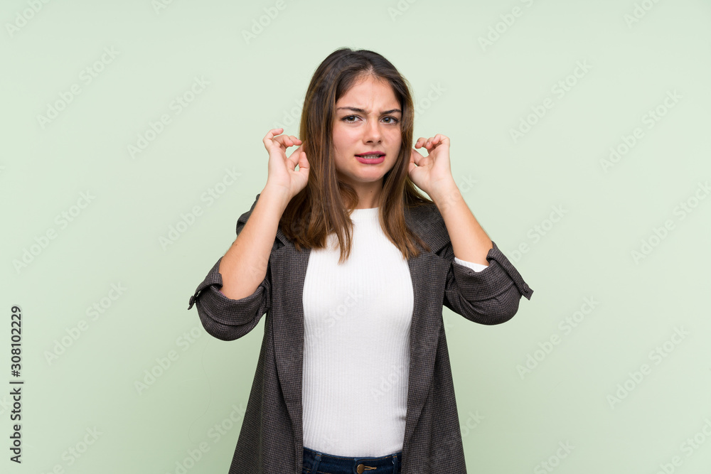 Young brunette girl with blazer over isolated green background frustrated and covering ears Young brunette girl with blazer over isolated green background frustrated and covering ears